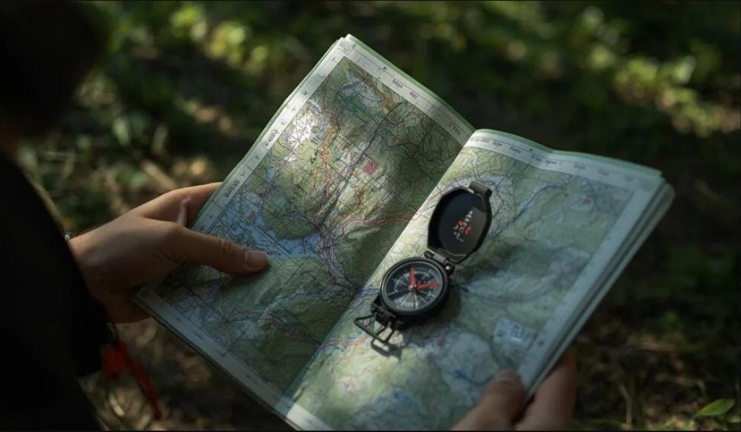 Hands holding an open topographic map with a compass resting on it in the woods