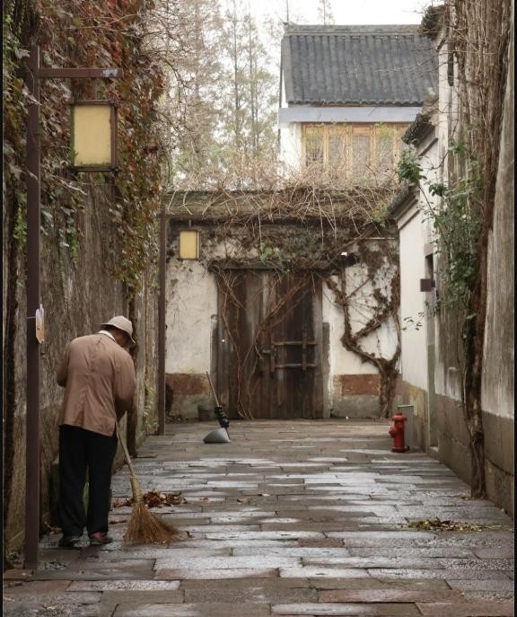 A person sweeping a stone alleyway between old ivy-covered buildings